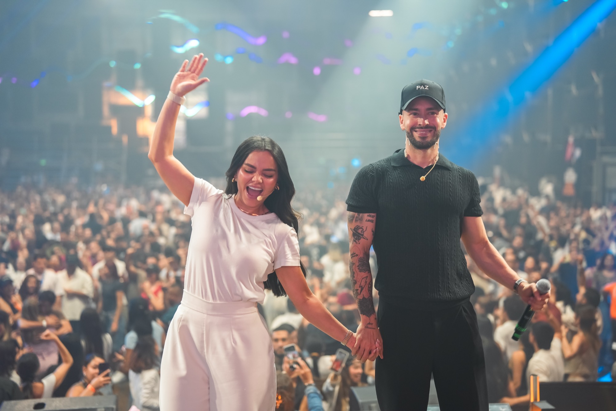 Valentina y Javi de la mano en el escenario, sonriendo y saludando al público