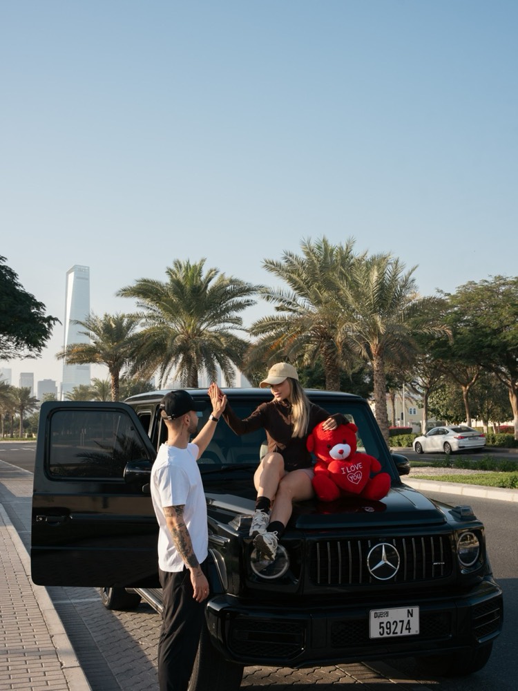 Valentina y Javi chocando la mano junto a su coche, con un peluche rojo de I love you