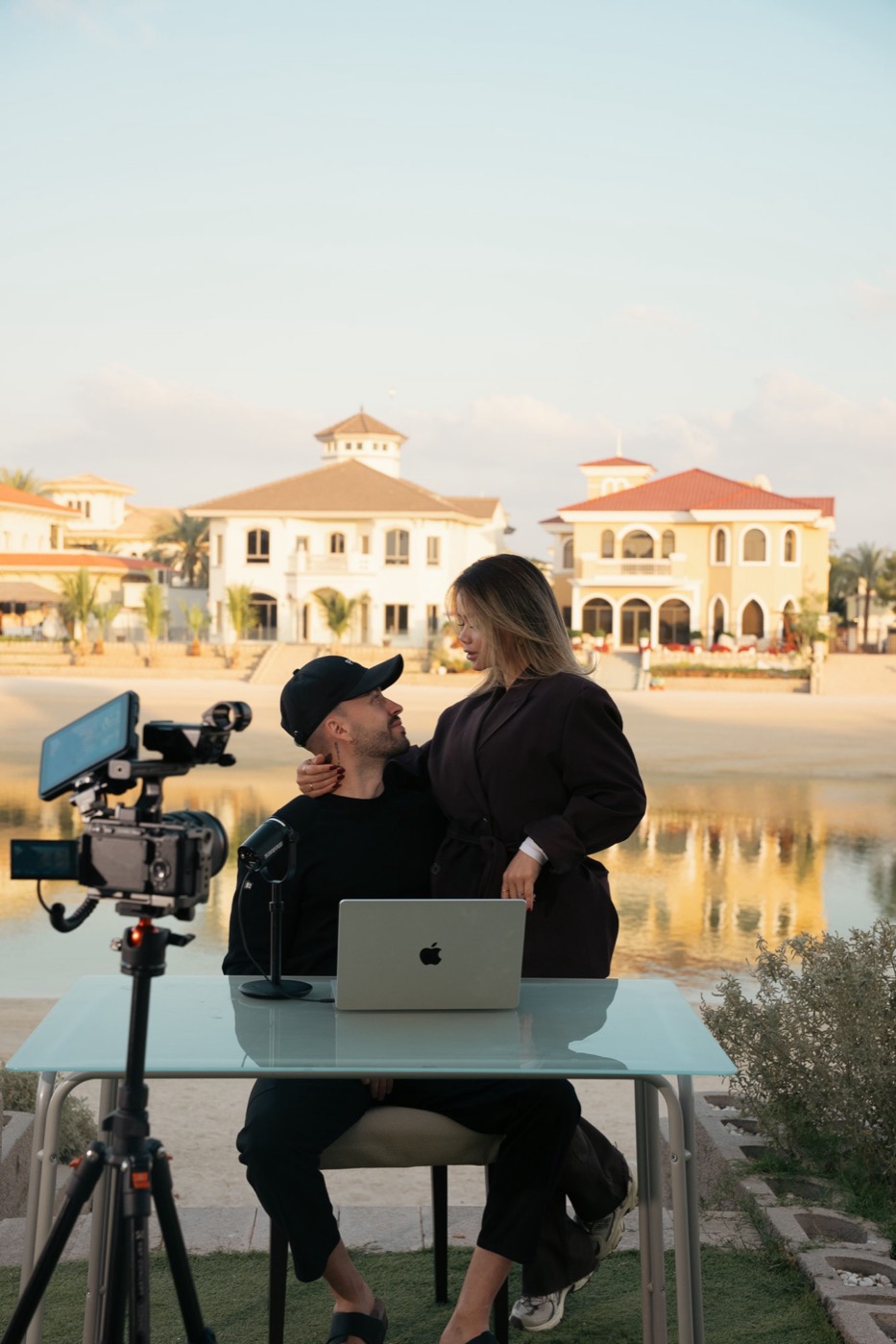 Valentina y Javi mirándose, trabajando juntos frente a unas villas junto al agua