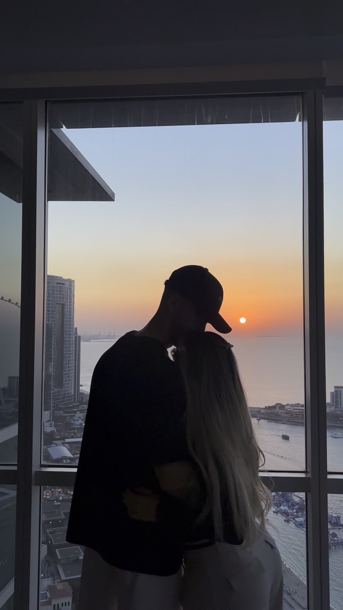 Valen y Javi abrazados frente a un ventanal al atardecer